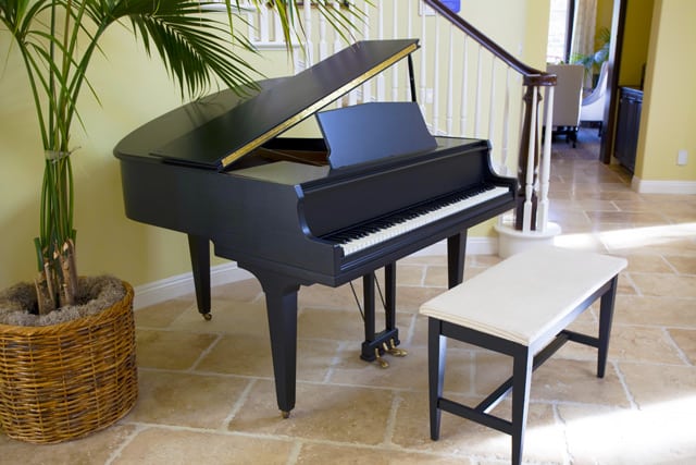 Black grand piano in front of a staircase next to a potted plant. 
